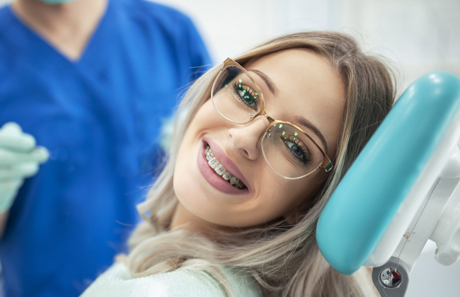 Young woman wearing glasses smiling in dental chair during orthodontic appointment