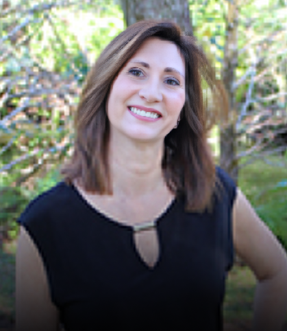 Woman smiling at camera wearing black shirt, outdoor setting with trees in background.