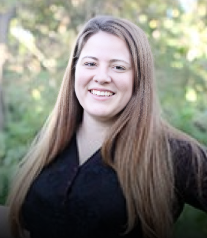 Professional portrait of smiling woman with long brown hair against blurred green outdoor background.