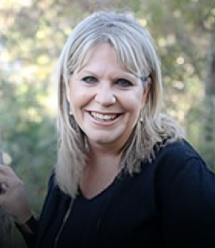 Professional headshot of smiling woman with blonde hair wearing black top, outdoor blurred background.