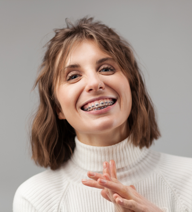 Smiling woman in white turtleneck against gray background for orthodontics practice headshot.