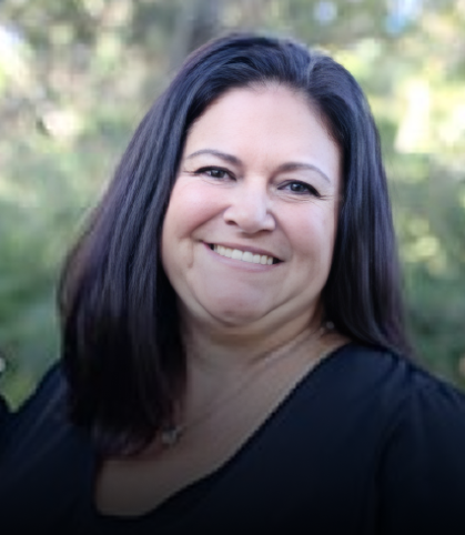Woman smiling at camera wearing black shirt, outdoor blurred green background, professional headshot.