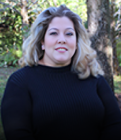Woman in black turtleneck smiling outdoors with trees in background.
