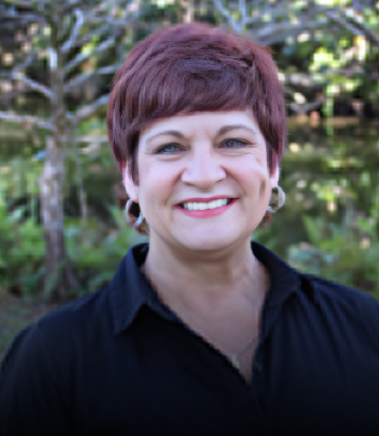 Woman with short burgundy hair smiling at camera outdoors in professional portrait for orthodontics practice.