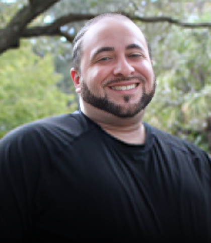 Man smiling outdoors in black shirt with tree branches in background.