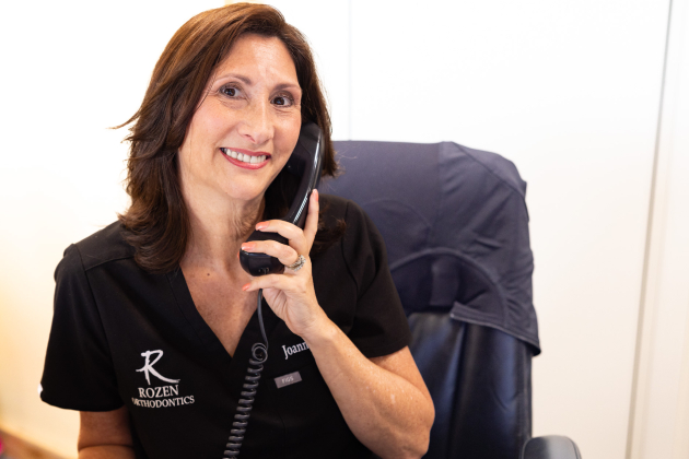 Woman in black Rozen Orthodontics polo shirt talking on phone at office desk.