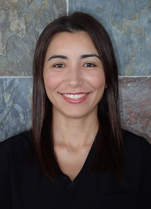 Professional headshot of smiling woman with long dark hair against textured blue-gray background.