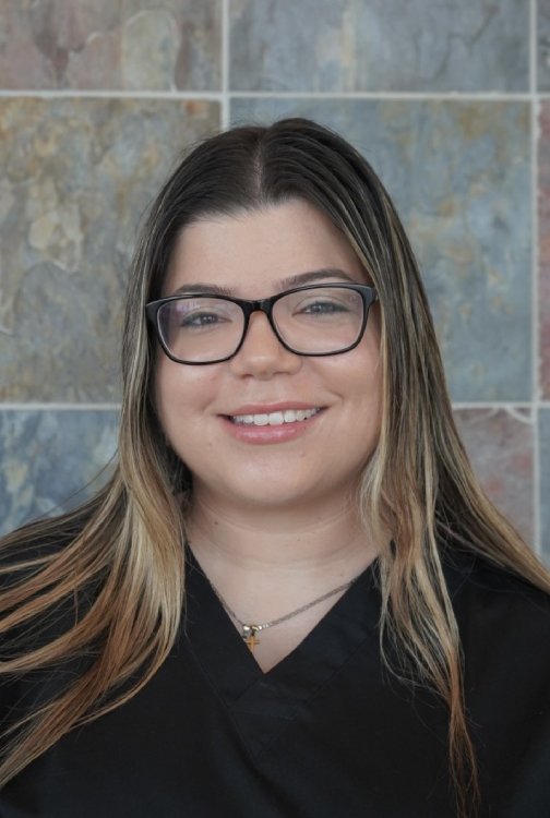 Professional headshot of smiling woman wearing glasses against tiled background for orthodontics practice.