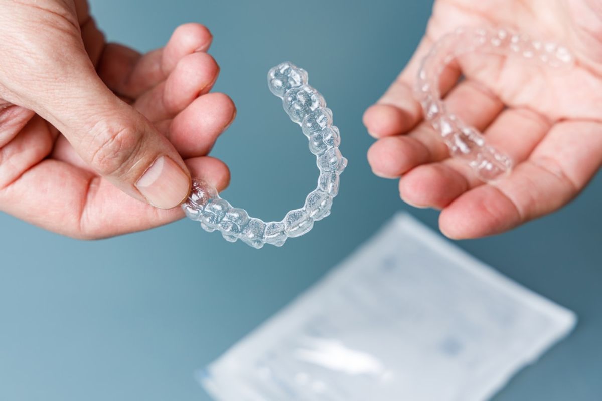 Hands holding clear orthodontic aligner against blue background with storage case below