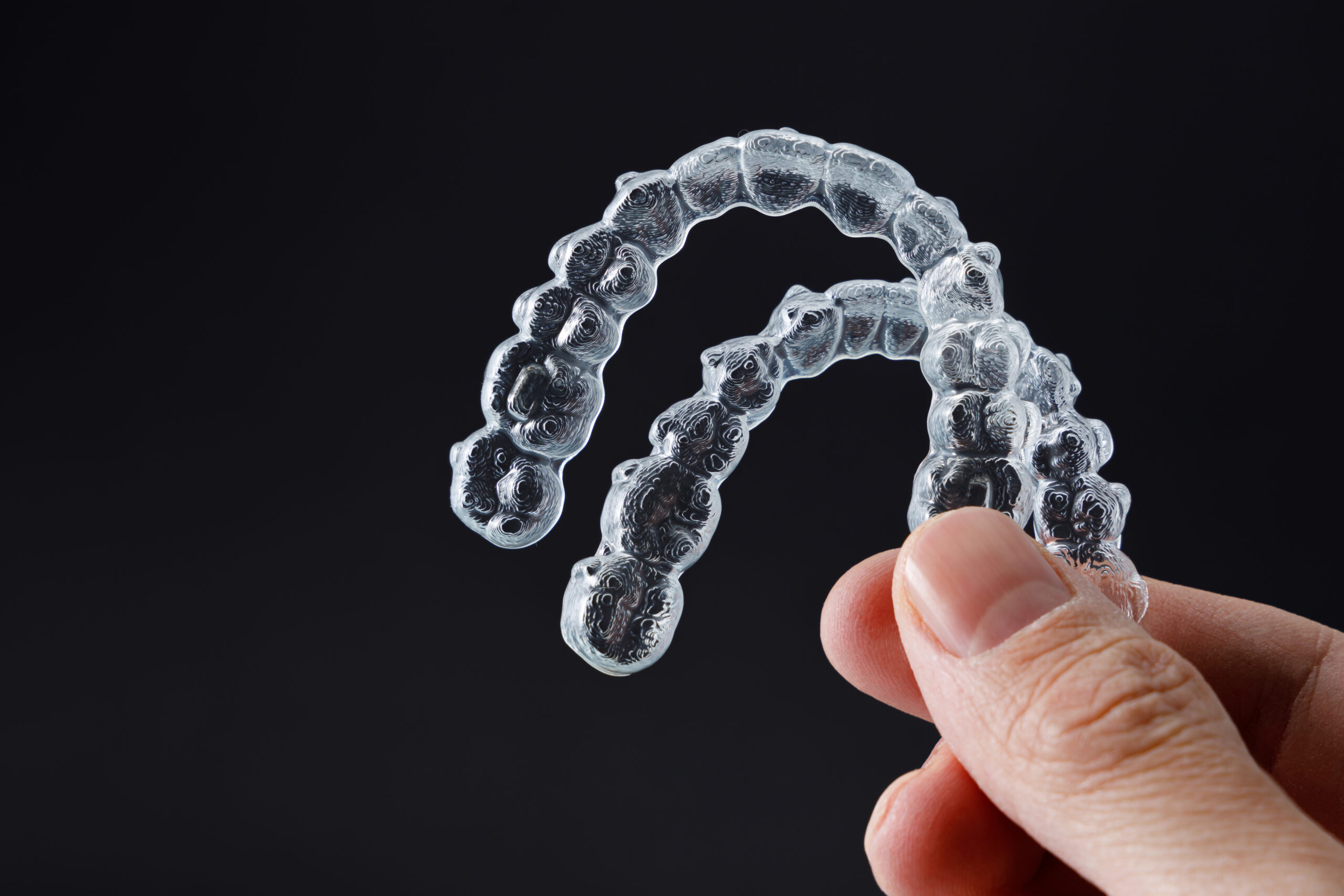Person holding clear orthodontic aligners against dark background for dental treatment demonstration.