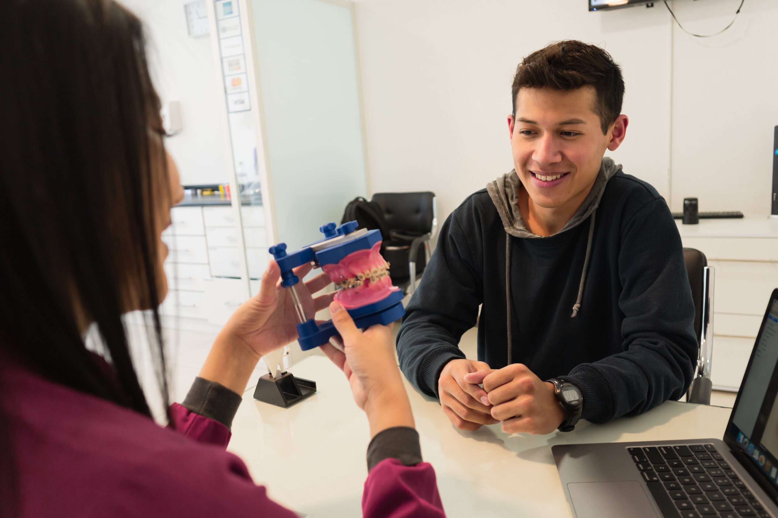 Man and woman examining red orthodontic model at dental office desk.