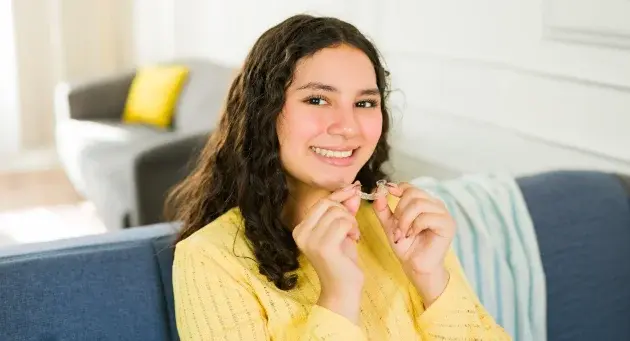 Smiling teen girl wearing yellow shirt in dental office setting with Invisalign aligners.